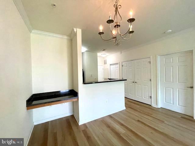 kitchen featuring dark countertops, wood finished floors, baseboards, an inviting chandelier, and ornamental molding