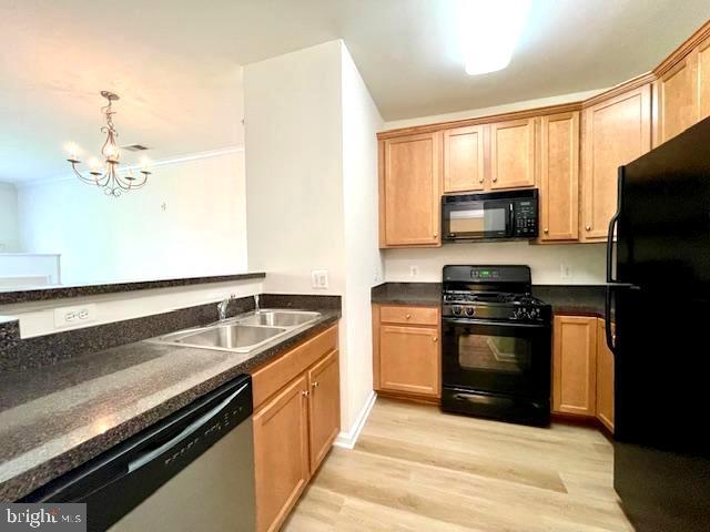 kitchen featuring dark countertops, light wood-type flooring, a sink, black appliances, and a notable chandelier
