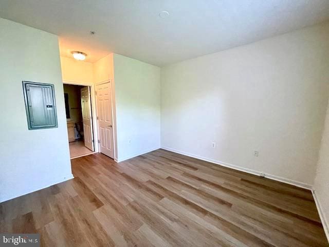 unfurnished room featuring baseboards, electric panel, and wood finished floors