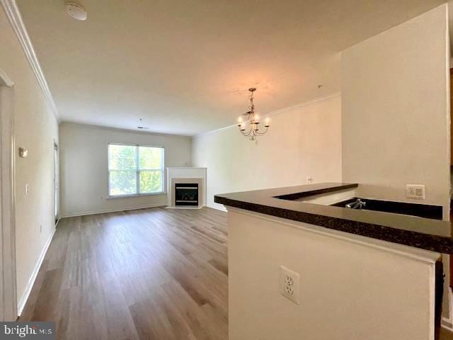 unfurnished living room featuring a fireplace, wood finished floors, baseboards, a chandelier, and ornamental molding
