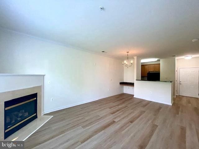 unfurnished living room with a glass covered fireplace, baseboards, wood finished floors, and a chandelier