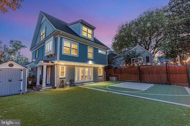 back of property at dusk with fence, a storage unit, french doors, an outdoor structure, and a lawn