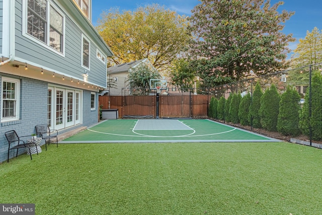 view of basketball court featuring a lawn, fence, and basketball court