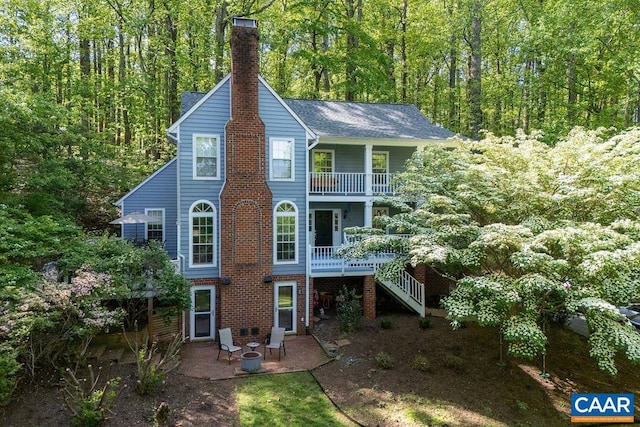 back of house featuring a chimney, stairway, a wooded view, a balcony, and a patio