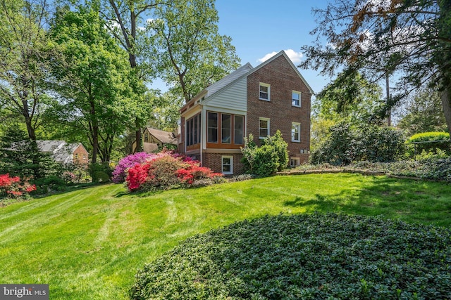 back of house with a yard, a sunroom, and brick siding