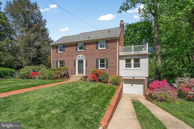 colonial inspired home with brick siding, a front yard, a chimney, a balcony, and driveway