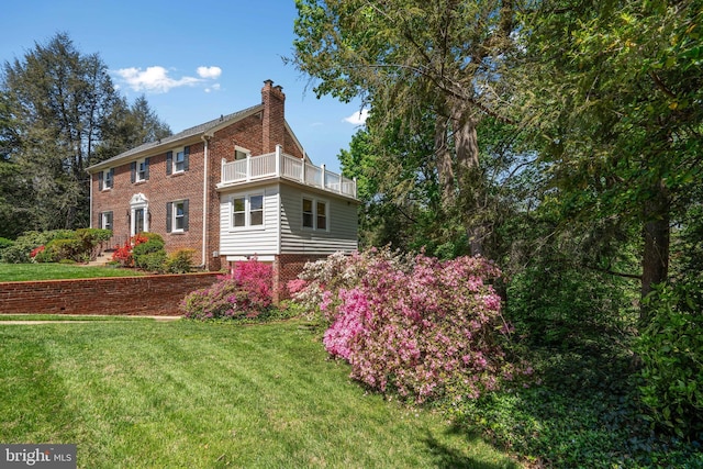 view of property exterior with a lawn, a chimney, brick siding, and a balcony