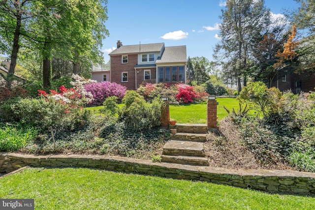 rear view of property featuring a lawn, brick siding, a chimney, and a sunroom
