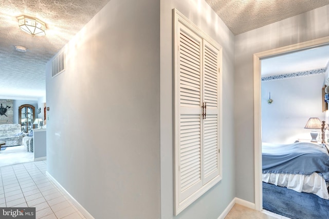 hall with light tile patterned flooring, a textured ceiling, visible vents, and baseboards