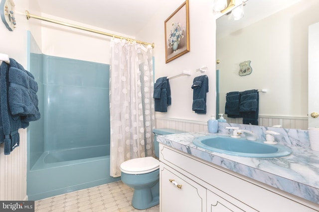 full bath with vanity, toilet, tile patterned floors, shower / bathtub combination with curtain, and a wainscoted wall