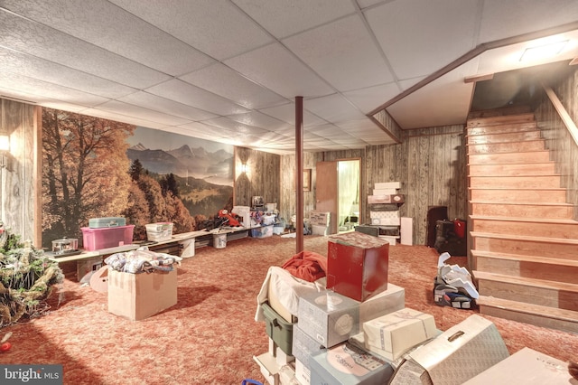 basement with wooden walls, carpet, a paneled ceiling, and stairway