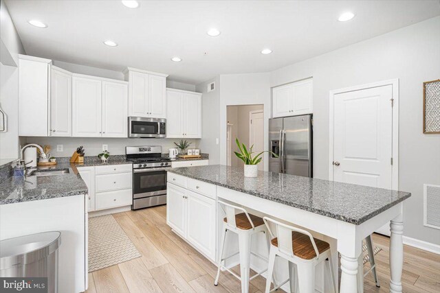 kitchen with appliances with stainless steel finishes, a center island, light wood-type flooring, a sink, and white cabinetry
