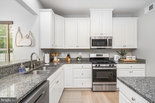 kitchen featuring visible vents, dark stone counters, white cabinetry, a sink, and appliances with stainless steel finishes
