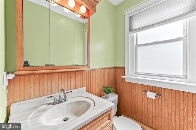 bathroom featuring vanity, wainscoting, wooden walls, and toilet