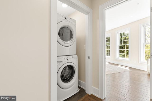 washroom featuring baseboards, stacked washer / drying machine, dark wood finished floors, and laundry area