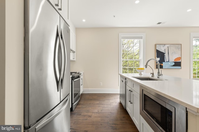 kitchen featuring baseboards, dark wood-type flooring, white cabinets, a sink, and stainless steel appliances