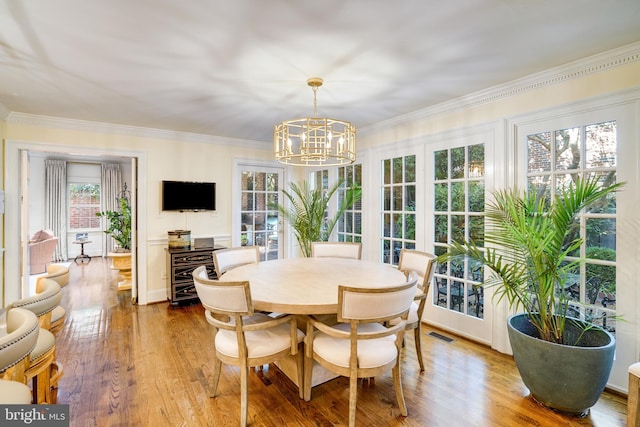 dining space with an inviting chandelier, crown molding, wood finished floors, and visible vents