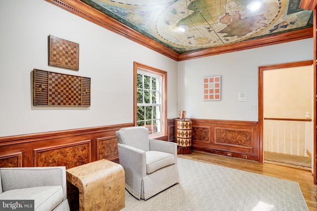 living area with ornamental molding, wood finished floors, and a wainscoted wall