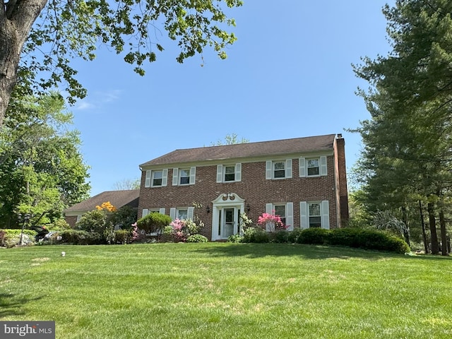 colonial inspired home with brick siding, a chimney, and a front yard