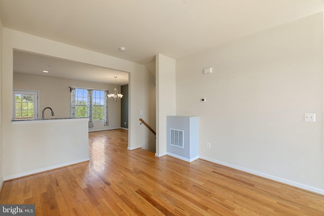 empty room with visible vents, light wood-style floors, baseboards, a sink, and a notable chandelier