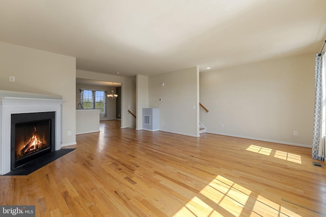 unfurnished living room with a fireplace with flush hearth, light wood-type flooring, stairway, baseboards, and a chandelier