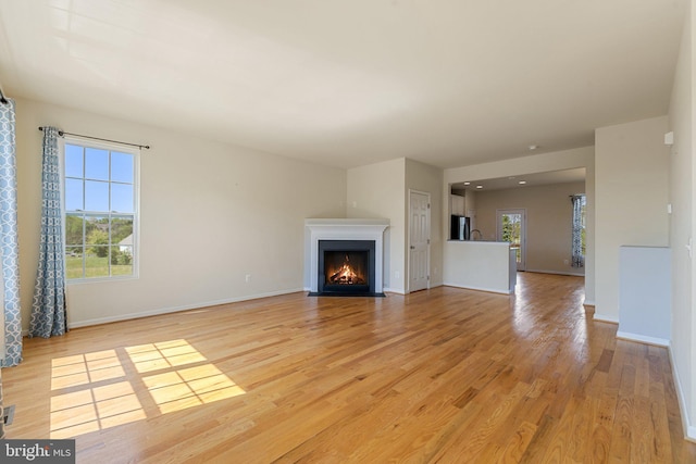 unfurnished living room featuring a fireplace with flush hearth, baseboards, and light wood finished floors