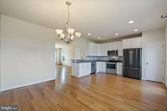 kitchen featuring white cabinets, dark countertops, light wood-style flooring, stainless steel appliances, and decorative backsplash