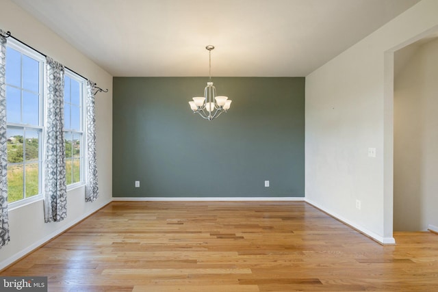 unfurnished dining area featuring an inviting chandelier, baseboards, and light wood-type flooring