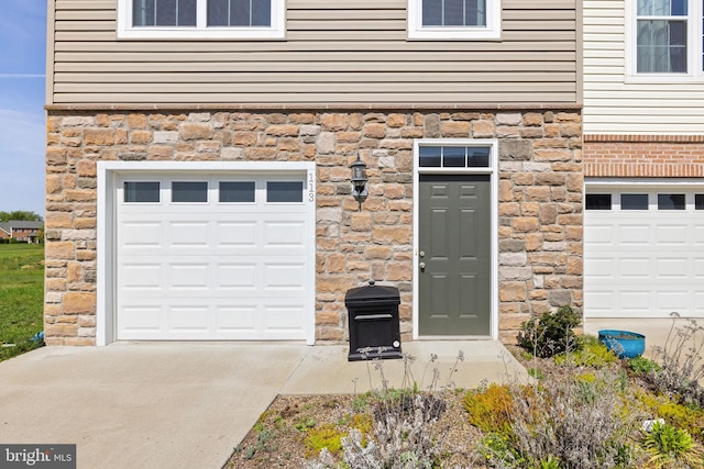 entrance to property with driveway, stone siding, and a garage
