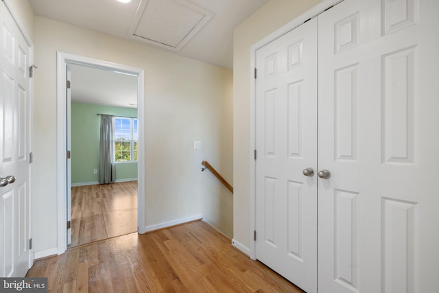 corridor featuring baseboards, attic access, light wood finished floors, and an upstairs landing