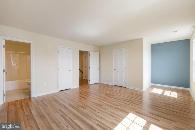 unfurnished bedroom featuring baseboards, light wood-style flooring, and ensuite bath