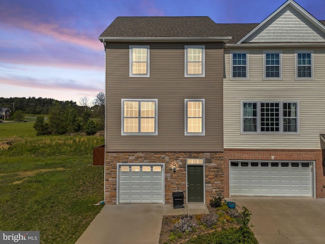 multi unit property with a lawn, concrete driveway, an attached garage, a shingled roof, and stone siding