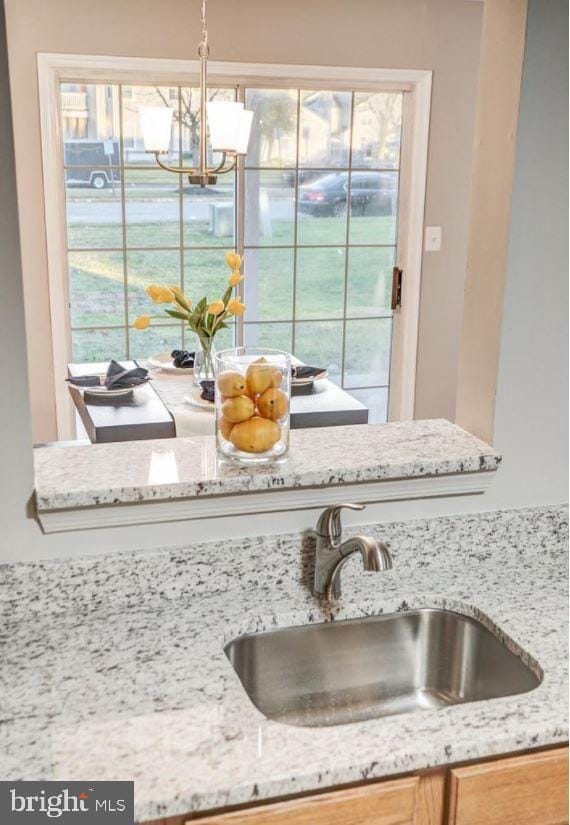 room details featuring light stone counters, a sink, and a chandelier