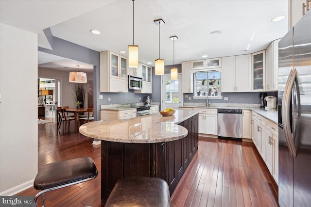 kitchen featuring a kitchen island, stainless steel appliances, light stone countertops, and dark wood finished floors