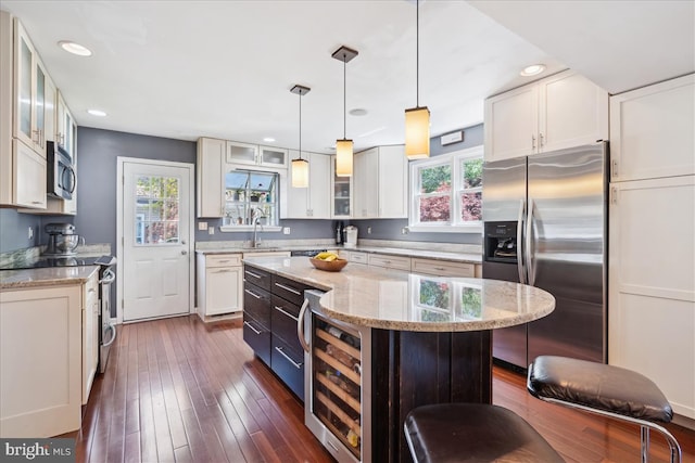 kitchen with white cabinets, appliances with stainless steel finishes, light stone counters, wine cooler, and a kitchen island