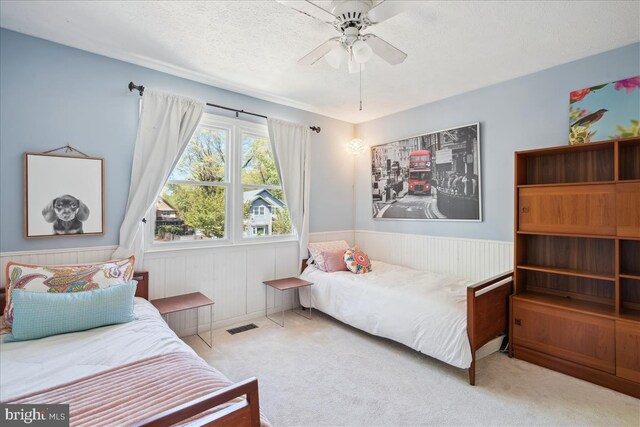 bedroom with visible vents, wainscoting, ceiling fan, a textured ceiling, and carpet flooring
