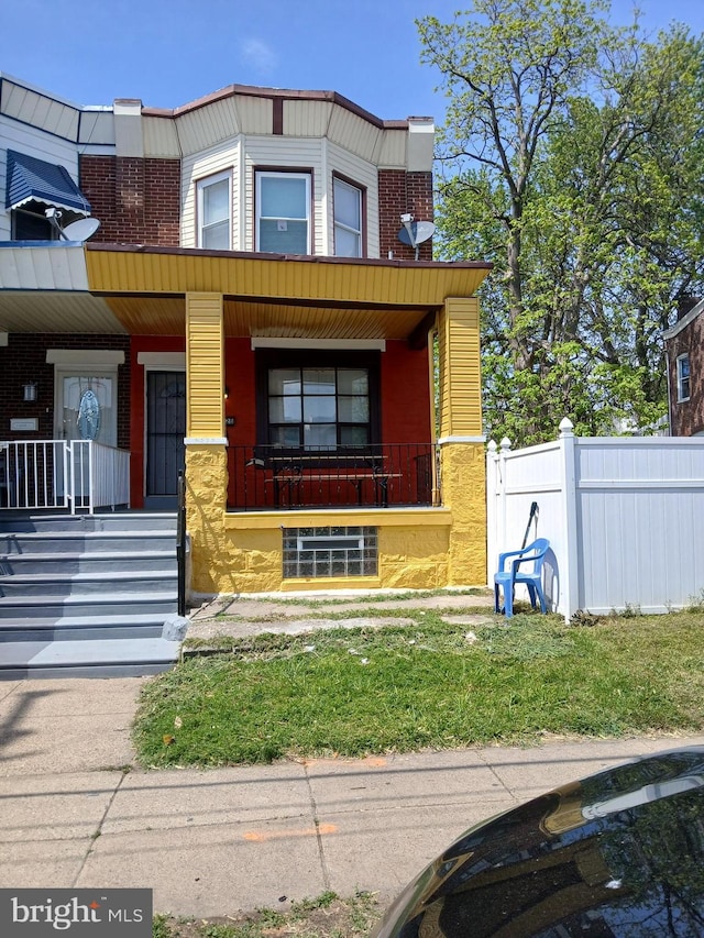 view of front facade with a porch, fence, and brick siding