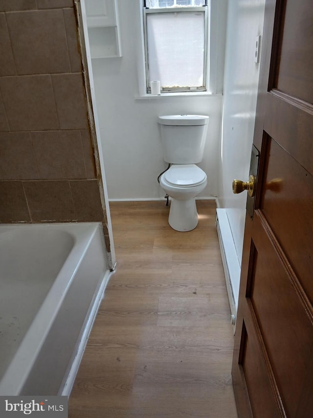 bathroom with a tub, wood finished floors, baseboards, a baseboard heating unit, and toilet