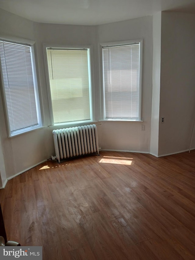 spare room with radiator heating unit, baseboards, and wood finished floors