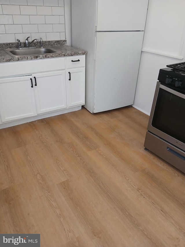 kitchen with a sink, light wood-style floors, white cabinets, and freestanding refrigerator
