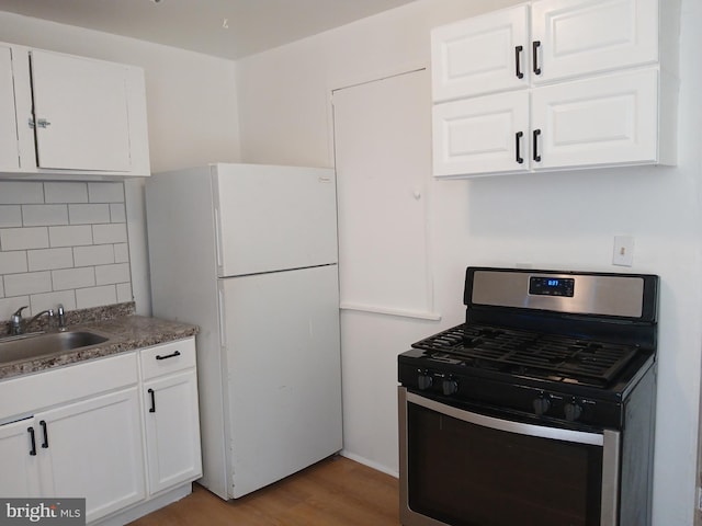 kitchen featuring decorative backsplash, a sink, stainless steel gas range, freestanding refrigerator, and light wood-style flooring