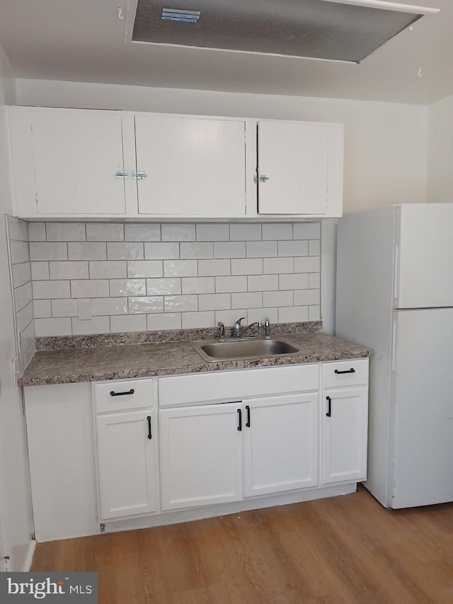 kitchen featuring freestanding refrigerator, white cabinets, a sink, and light wood-style floors