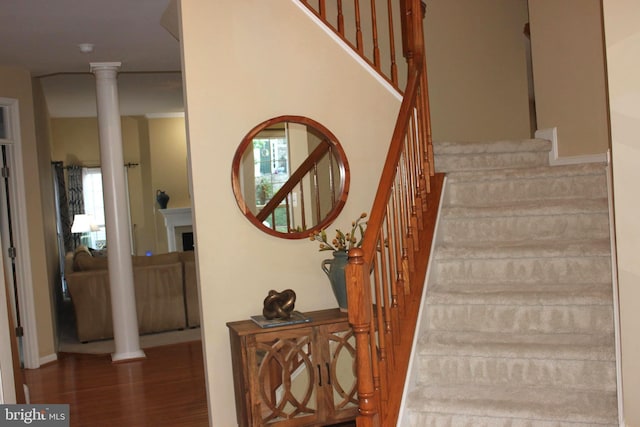 stairway with ornate columns, wood finished floors, and a healthy amount of sunlight