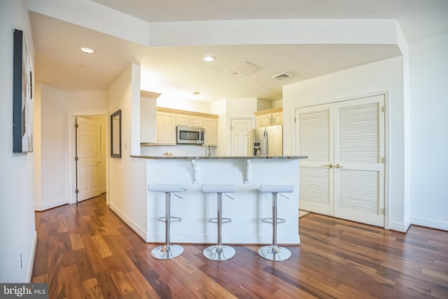 kitchen with a kitchen breakfast bar, appliances with stainless steel finishes, wood finished floors, baseboards, and stone countertops