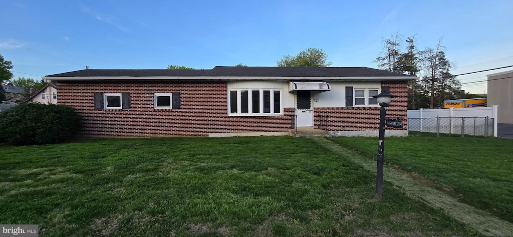 single story home featuring brick siding, fence, and a front yard