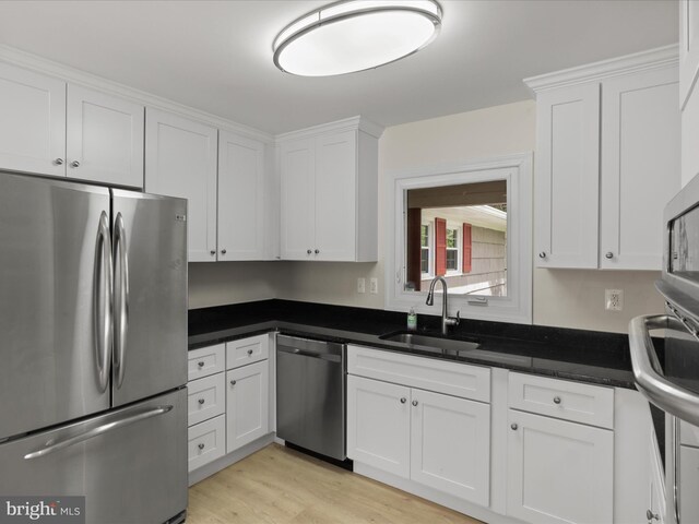 kitchen with dark countertops, a sink, white cabinets, stainless steel appliances, and light wood-style flooring