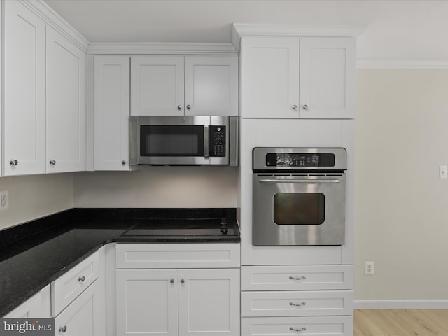 kitchen with white cabinets, appliances with stainless steel finishes, ornamental molding, and dark stone countertops