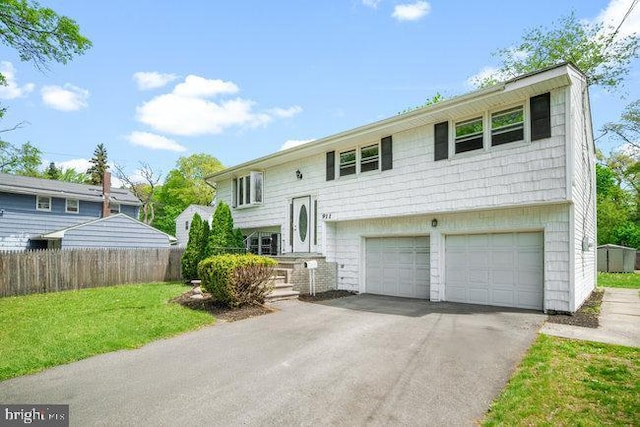 bi-level home featuring aphalt driveway, fence, a garage, and a front yard
