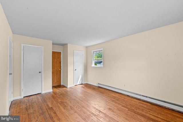 unfurnished bedroom featuring wood finished floors, baseboards, and a baseboard heating unit