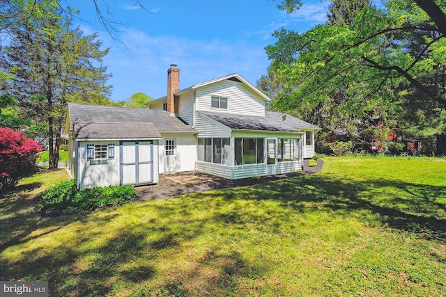 rear view of property featuring roof with shingles, a sunroom, a shed, a chimney, and a lawn